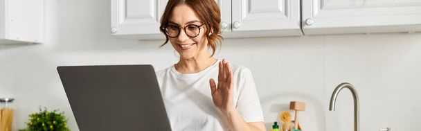 Frau mittleren Alters mit Brille steckt zu Hause in Laptop. - Foto, Bild