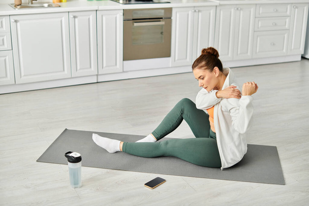 Жінка середнього віку знаходить спокій на йога килимок на кухні. - Фото, зображення
