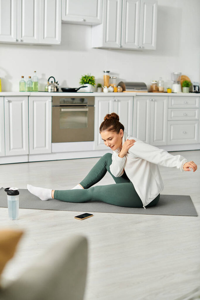 Kobieta w średnim wieku z wdziękiem ćwiczy jogę na macie w kuchni. - Zdjęcie, obraz