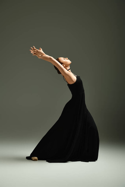 Μια νεαρή όμορφη μπαλαρίνα γοητευτικά χτυπά μια χορευτική στάση σε ένα μαύρο φόρεμα. - Φωτογραφία, εικόνα