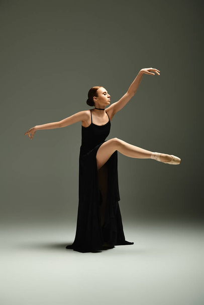 Η νεαρή, όμορφη μπαλαρίνα δείχνει το ταλέντο της σε μια δυναμική χορευτική πόζα φορώντας ένα μαύρο φόρεμα.. - Φωτογραφία, εικόνα