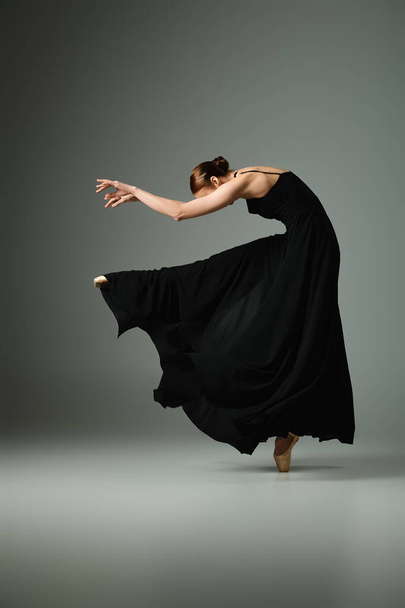 Μια νεαρή, όμορφη μπαλαρίνα με μαύρο φόρεμα να χορεύει με χάρη.. - Φωτογραφία, εικόνα