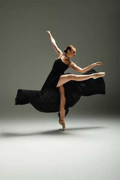 Fiatal, gyönyörű balerina kecsesen táncol fekete ruhában.. - Fotó, kép