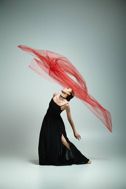 A young woman in a black dress gracefully holds a red veil. - Photo, Image