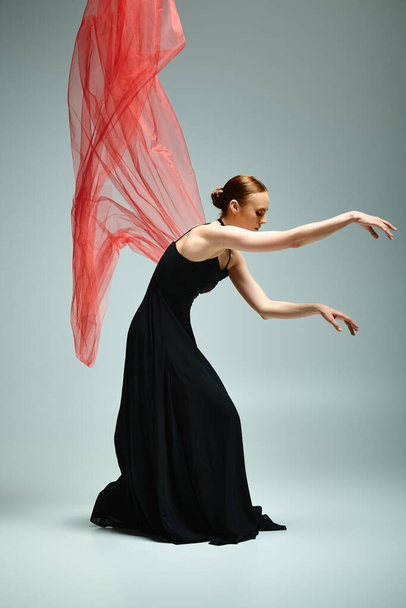 Egy fiatal, gyönyörű balerina fekete ruhában, kecsesen mozog vörös fátyollal.. - Fotó, kép