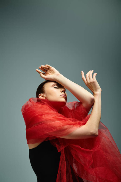 Young ballerina gracefully moves in a striking black dress and red shawl. - Photo, Image