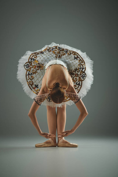 Eine junge, schöne Ballerina im weißen Tutu beugt sich anmutig vor. - Foto, Bild