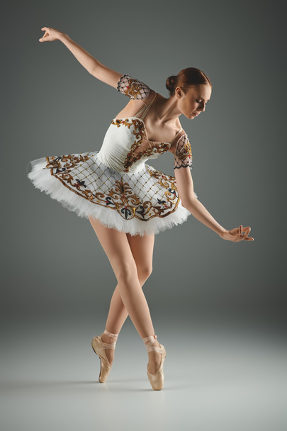 Młoda, utalentowana balerina z wdziękiem tańczy w białej spódniczce ze złotymi zdobieniami. - Zdjęcie, obraz