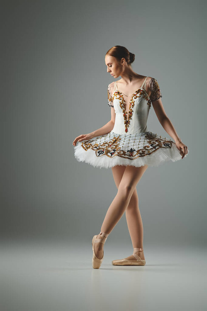 Een jonge ballerina beweegt sierlijk in een prachtige witte en gouden jurk. - Foto, afbeelding