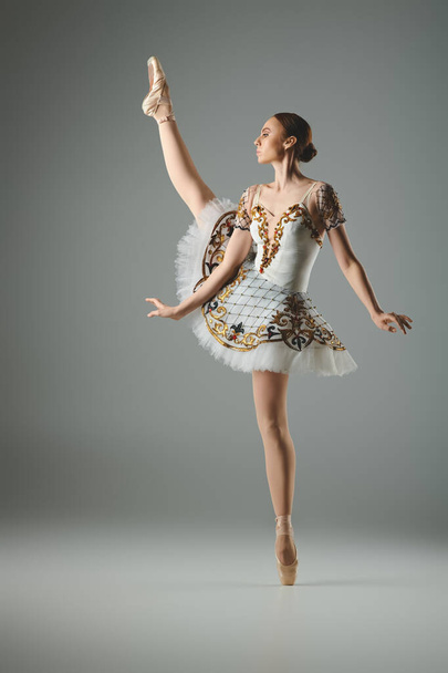 Młoda, piękna balerina tańczy energicznie w oszałamiającej białej i złotej sukience. - Zdjęcie, obraz