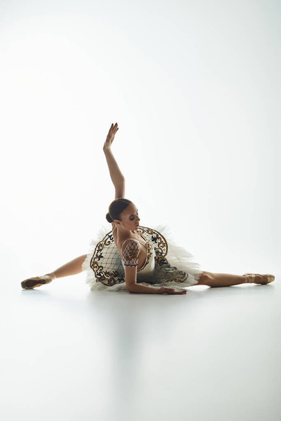 Fiatal gyönyörű balerina fehér ruhában, dinamikus táncpózt üt.. - Fotó, kép