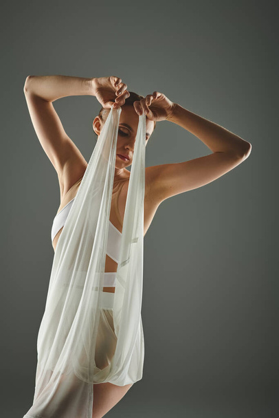 Молодая балерина в белом платье изящно держит вуаль над головой. - Фото, изображение