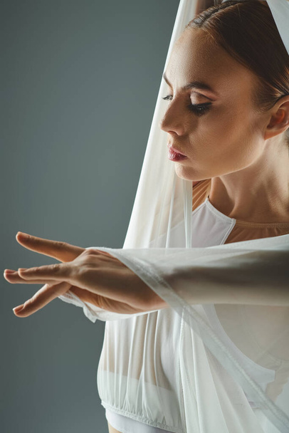 Nuori ballerina esittelee armoa ja ryhtiä valkoisessa mekossa, joka ulottuu hänen käsiinsä sulavasti.. - Valokuva, kuva