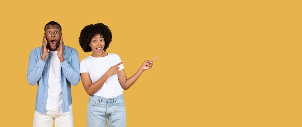 Abartılı ifadeleri olan afro-amerikan bir çift, yanaklarında elleri olan bir adam ve yanakları gösteren bir kadın, ikisi de hardal sarısı arka planda, panorama - Fotoğraf, Görsel