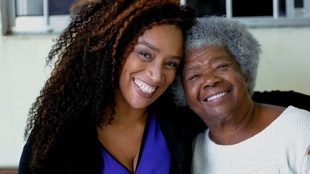 Szczęśliwy portret dorosłej Afroamerykanki z ręką wokół starszej, siwej matki z lat 80-tych. Zbliżenie twarzy radosnych międzypokoleniowych kobiet z ramieniem wokół ramienia - Zdjęcie, obraz