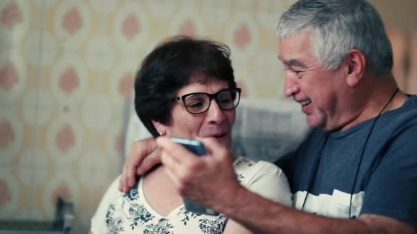Sposati anziani che reagiscono al messaggio di notifica positiva sul dispositivo cellulare, marito anziano con braccio intorno al coniuge che mostra il telefono e celebra insieme - Filmati, video