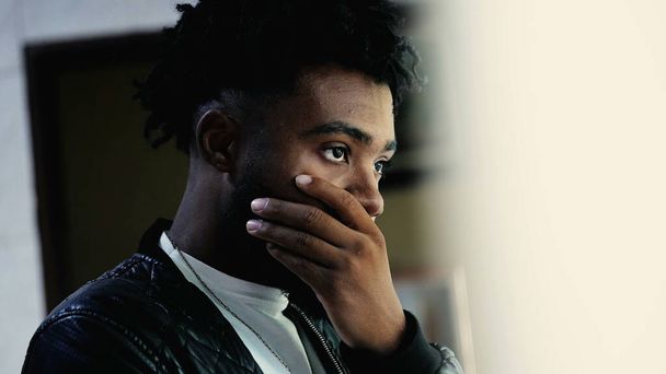 Yksi huolestunut nuori musta seisoo ikkunassa hiljaisessa mietiskelyssä pohtimassa ratkaisua ongelmaan. Pensive Person Afrikkalainen syntyperä tunne eksynyt ajatuksen peittää suu huolenaihe - Valokuva, kuva