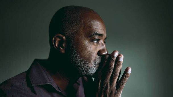 Yksi uskonnollinen musta vanhempi mies mietiskelevä PRAYER kotona hämärässä huoneessa silmät kiinni ottaa HOPE ja FAITH haastavina aikoina. Hengellinen Afrikkalainen Amerikan 50s henkilö - Valokuva, kuva