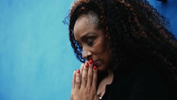 One worried hispanic black woman seeking solace during hard times Praying to GOD in urban setting gazing upwards with HOPE and FAITH - Photo, Image
