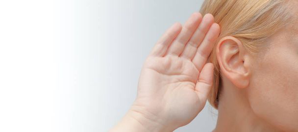 Jeune femme avec prothèse auditive sur fond clair. Dame avec prothèse auditive mettre sa main à son oreille - Photo, image