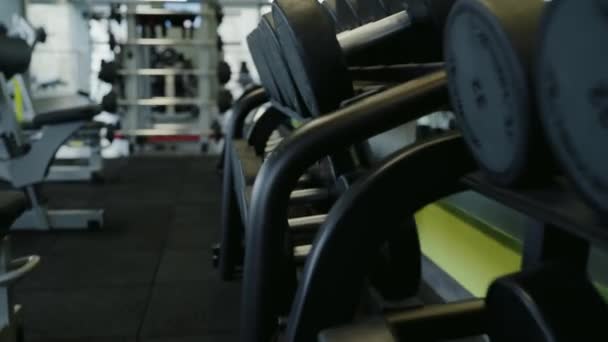 Interior do clube de fitness com halteres de ferro diferentes para treino ou treinamento de peso. Fechar em rack com equipamento desportivo no ginásio moderno. - Filmagem, Vídeo
