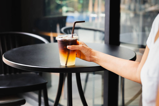 Mulher bebendo café gelado em taça de plástico takeaway na mesa de café ao ar livre - Foto, Imagem