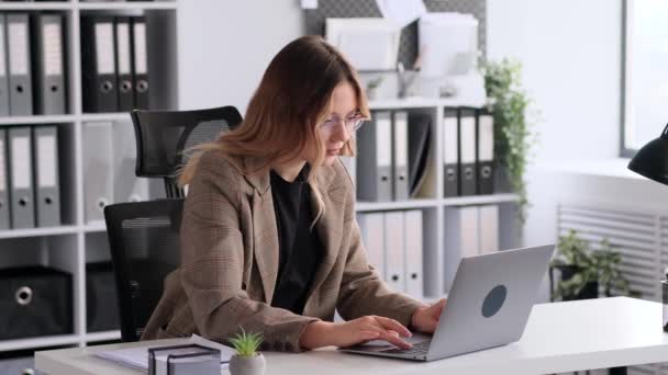 Portrait of a successful and smiling young Caucasian businesswoman or accountant working with laptop in office. Female boss or chief looking at camera. - Footage, Video