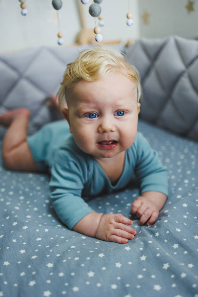 6 aylık bir çocuk beşiğinde yatar ve kameraya bakar. Bebek yatağı için gri çarşaf. - Fotoğraf, Görsel