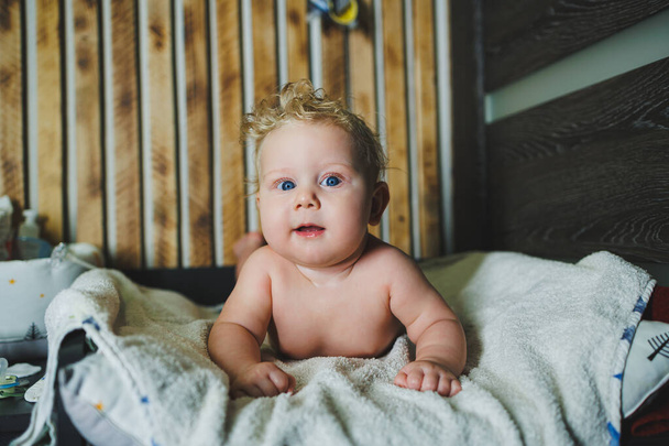 Kędzierzawy noworodek leży na białym ręczniku po kąpieli. Portret 6-miesięcznego dziecka z uśmiechem na twarzy. - Zdjęcie, obraz