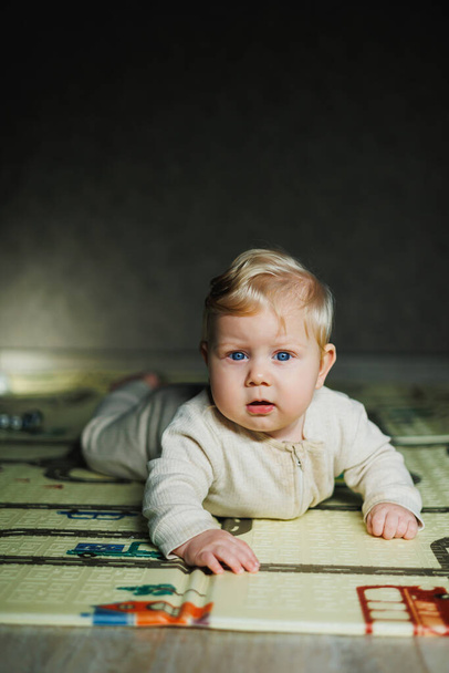 El niño se arrastra sobre su estómago. Un pequeño bebé de 6 meses se arrastra sobre la alfombra y sonríe. Un niño juega con un juguete en el suelo. - Foto, imagen