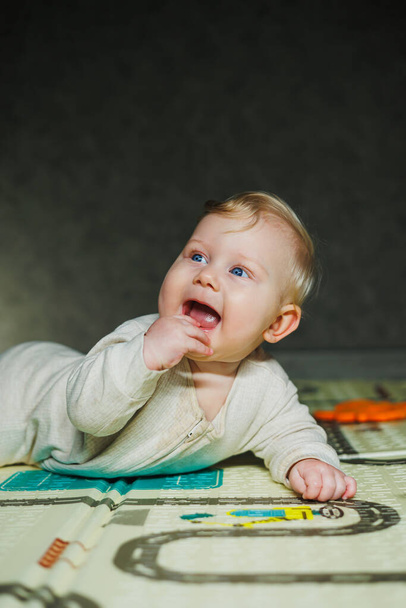 A criança rasteja sobre o estômago. Um pequeno bebê de 6 meses está rastejando no tapete e sorrindo. Um menino brinca com um brinquedo no chão. - Foto, Imagem