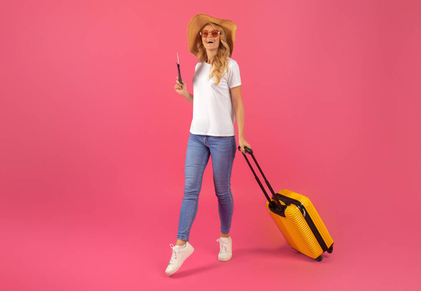 Відпустка Вібс. Блондинка мандрівник, що стоїть з багажем і квитками, сприяє радості подорожей, позує на рожевому студійному фоні, рекламує сезонні тури і страхування подорожей - Фото, зображення
