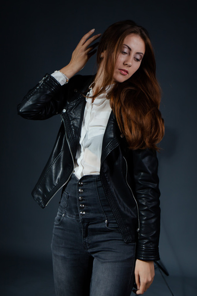 Glamorous young woman in black leather jacket on black background - Фото, изображение