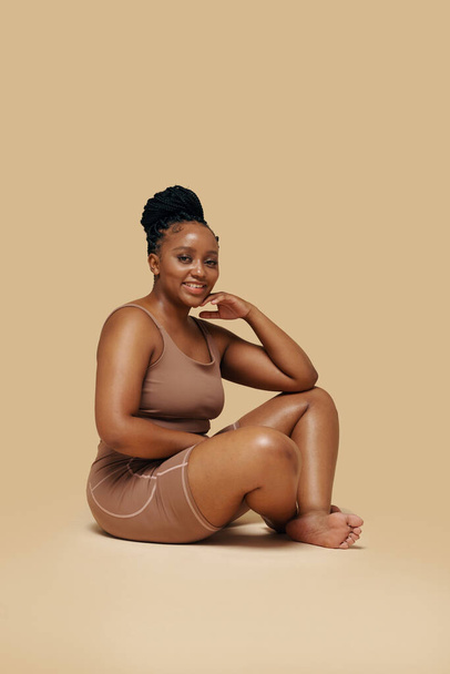 Studio portret van glimlachende ronding Zwarte vrouw in shapewear - Foto, afbeelding