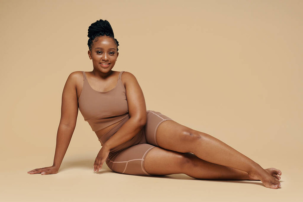 Sorrindo mulher negra em sportswear sentado no chão do estúdio - Foto, Imagem