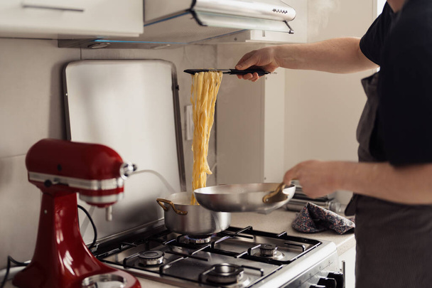 Человек приготовления спагетти в кастрюле из нержавеющей стали на газовой плите в аккуратной кухне. - Фото, изображение