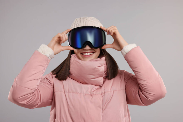 Winter sports. Happy woman with snowboard goggles on grey background - Photo, Image