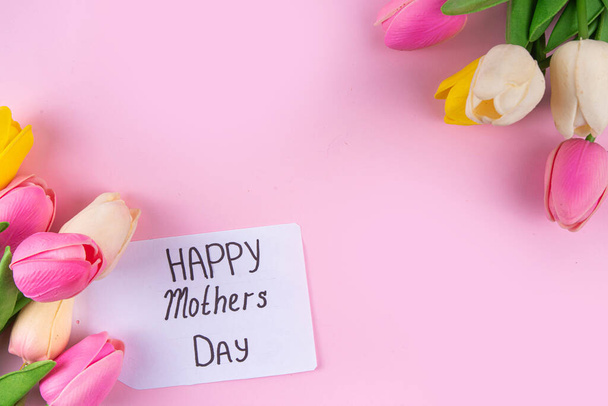 チューリップの花束,ピンクのリボンとハッピーマザーデーのタグが付いているギフト用の箱との母の日の背景. グリーティングカードの背景,ポスター,パンフレット,小冊子,プロモーション資料,ウェブサイトのフラットレイ - 写真・画像