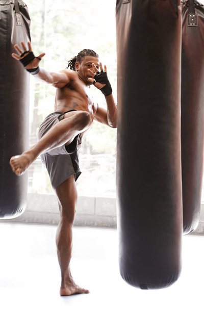 Ο άνθρωπος, λάκτισμα πυγμαχία και τσάντα με την κατάρτιση, τα πόδια και τη μάχη για την άσκηση με την ισορροπία, τη δύναμη και την ακρίβεια στο γυμναστήριο. Αφρικανός αθλητής, άτομο ή μαχητής με προπόνηση, φυσική κατάσταση ή απεργία για πρόκληση στο dojo. - Φωτογραφία, εικόνα