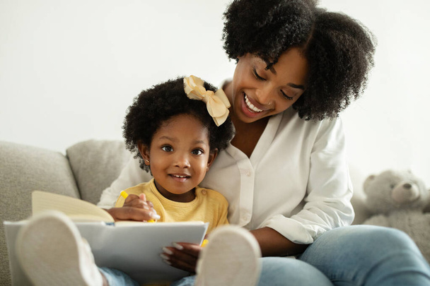 Développement du bébé. jolie jeune noir maman lecture livre avec son mignon bébé fille à la maison, heureux afro-américain mère passer du temps avec tout-petit enfant, profiter de congé de maternité, gros plan - Photo, image