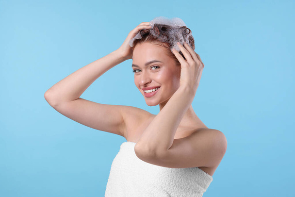 Happy young woman washing her hair with shampoo on light blue background - Valokuva, kuva