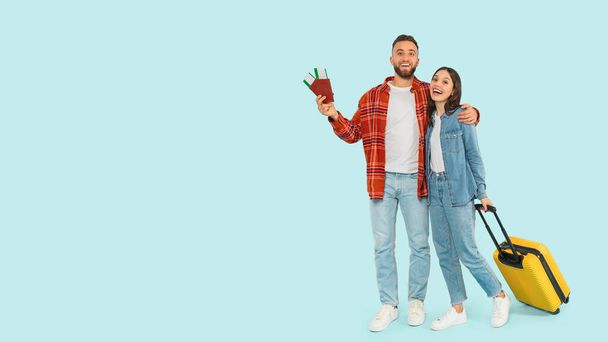 Happy Young Tourists Couple Ready For Vacation, Standing With Yellow Suitcase, Passports And Travel Tickets Over Blue Background In Studio, Full Length Shot, Panorama With Empty Space - Фото, зображення
