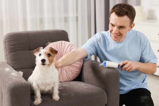 Smiling man removing pet's hair from armchair at home - Foto, Imagen
