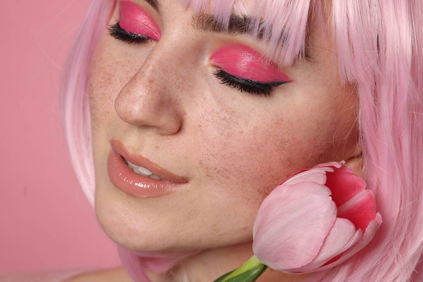 Beautiful woman with bright makeup, fake freckles and tulip on pink background, closeup - Foto, imagen