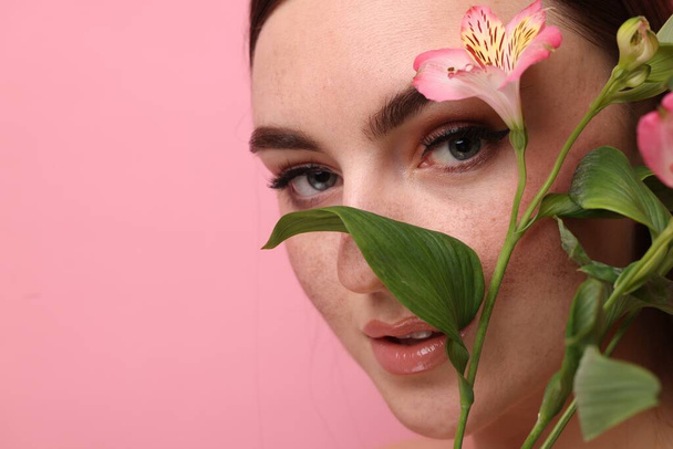 Beautiful woman with fake freckles and flower on pink background, closeup. Space for text - Foto, imagen