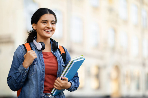 Pozitivní studentka z východu, pózuje na univerzitním kampusu, drží cvičebnice, nosí batoh, dívá se na kopírovací prostor a usmívá se. Vzdělání, škola, vysokoškolský koncept - Fotografie, Obrázek