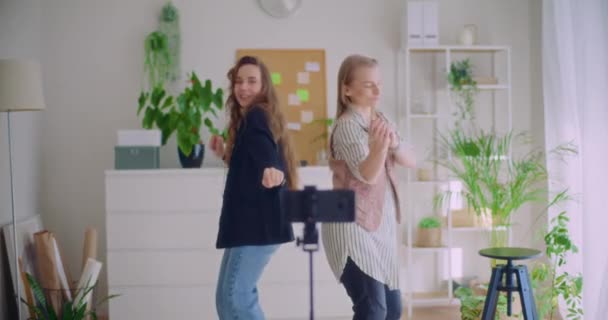 Zeitlupenaufnahme glücklicher junger Influencerinnen, die gemeinsam mit ihrem Smartphone auf einem Stativ zu Hause Tanzvideos aufnehmen - Filmmaterial, Video