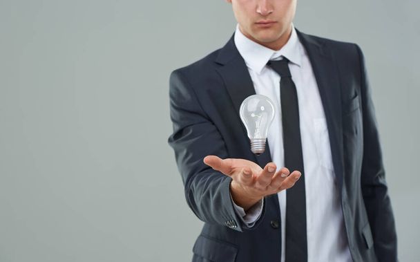 Business man, light bulb and ideas for company, entrepreneur with innovation and problem solving for energy saving. Hologram, solution and corporate goals for knowledge and power on grey background. - Photo, Image