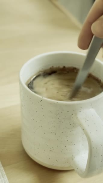 Egy csésze fehér kávé egy fából készült asztalon, amit teáskanállal helyeznek el.  - Felvétel, videó
