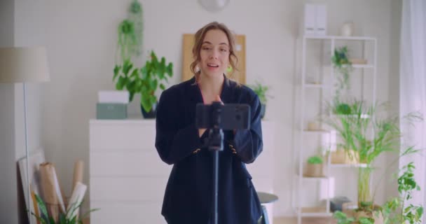 Αργή κίνηση της ευτυχούς νεαρή γυναίκα influencer vlogging μέσω smartphone στο τρίποδο στο σπίτι - Πλάνα, βίντεο